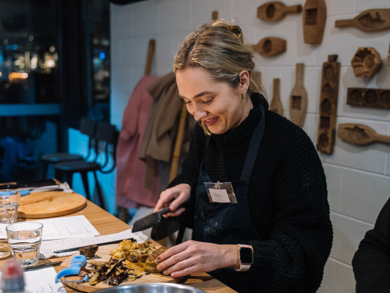 Woman smiling whilst chopping food at a cooking class.